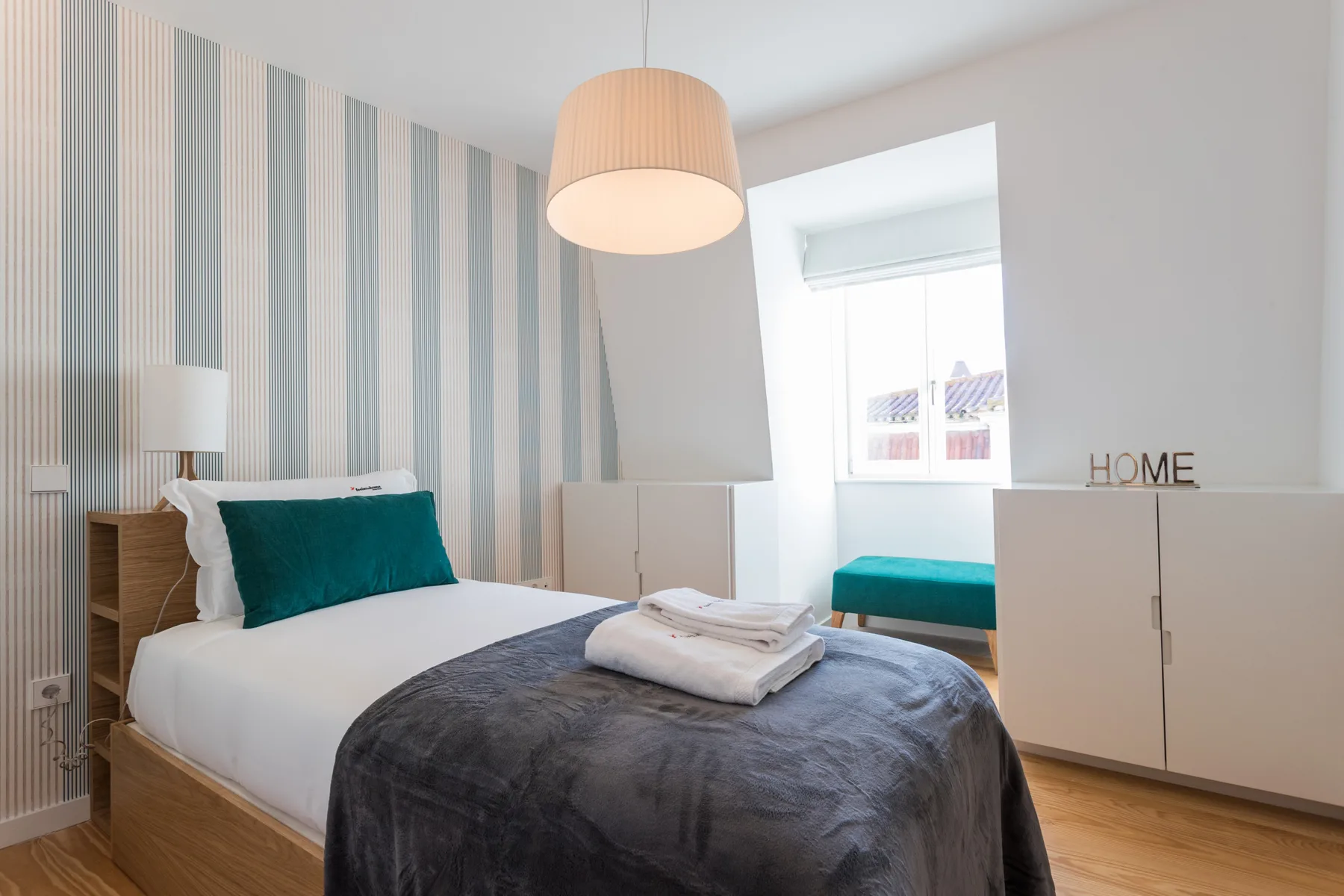 Dormitorio con una cama bien arreglada y papel pintado a rayas.