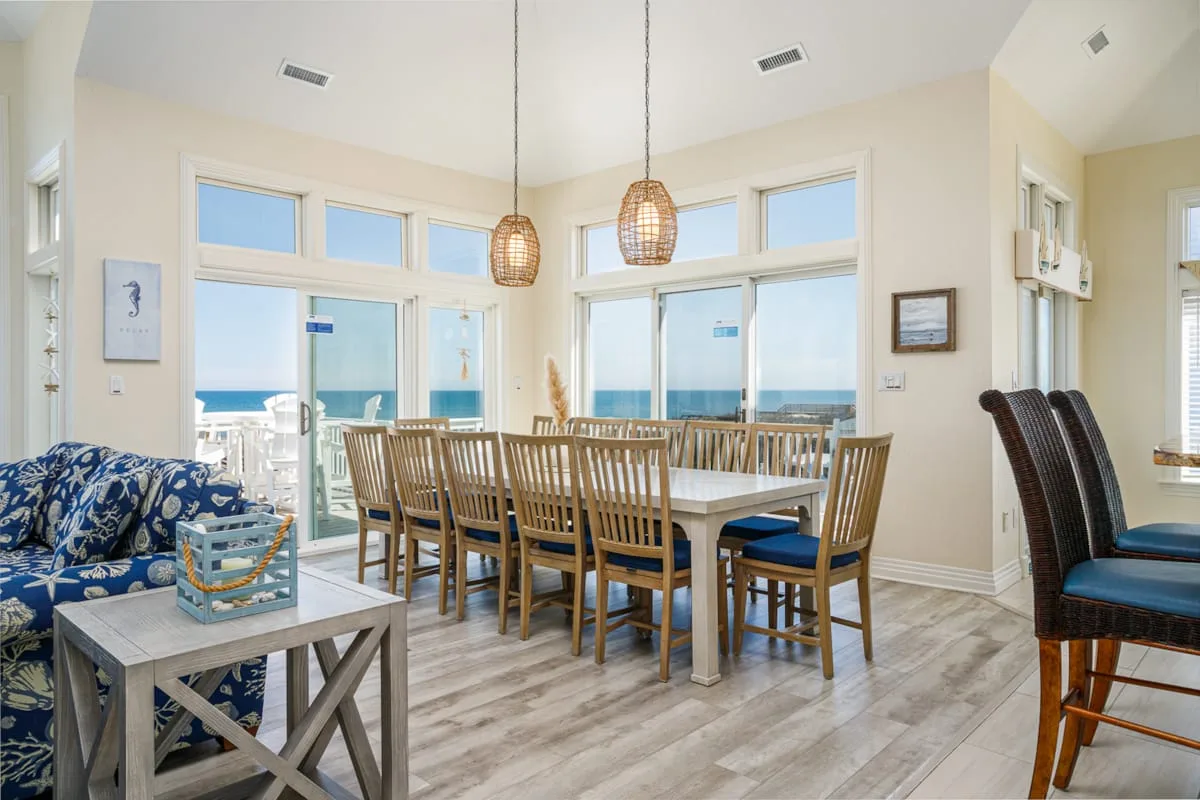 Un comedor luminoso con una mesa de madera y grandes ventanales con vistas al mar.