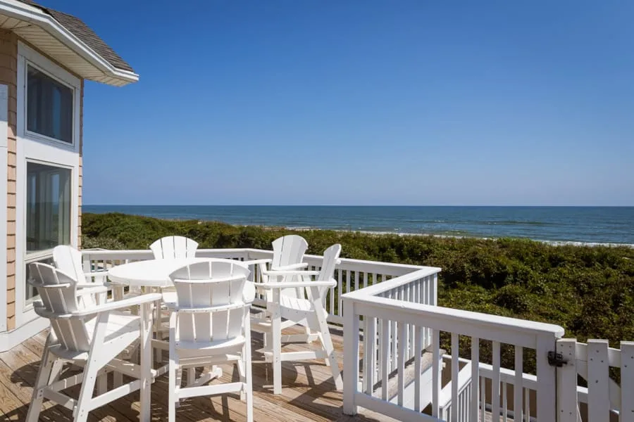 Una terraza junto al mar tiene asientos blancos con vistas al océano y vegetación costera.