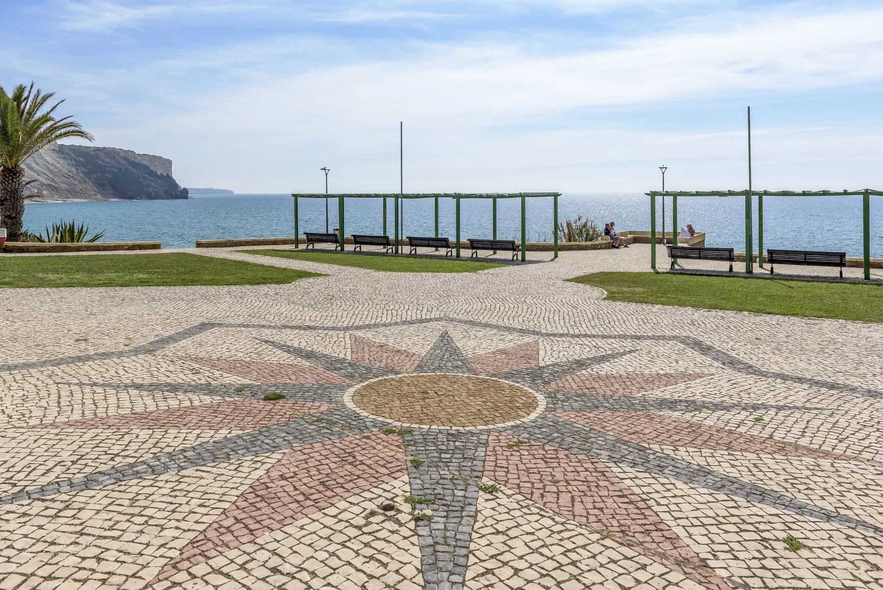 Un paseo junto al mar con pavimento decorativo, bancos y vistas al agua.
