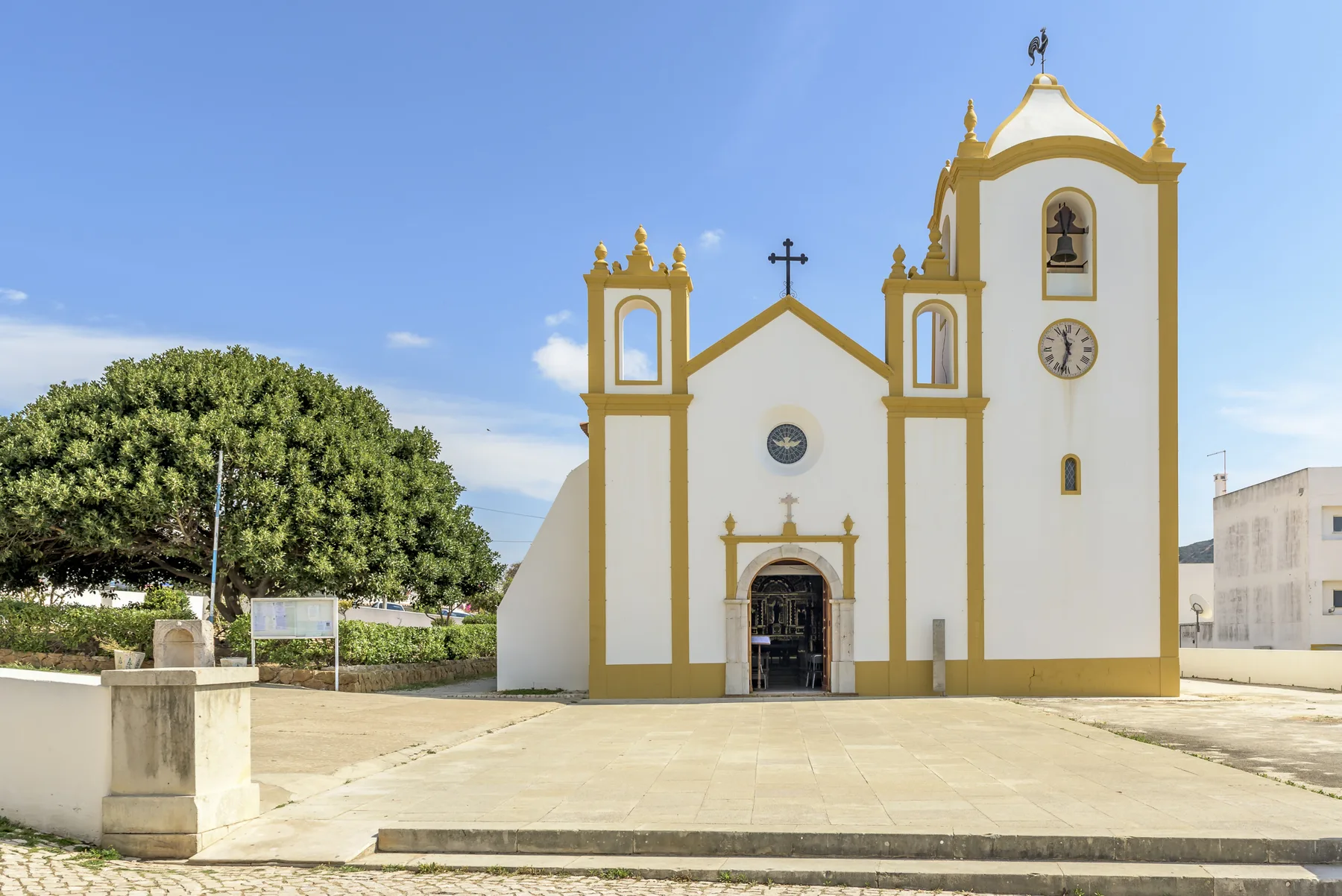 Una iglesia blanca con detalles amarillos da a una amplia plaza pavimentada.