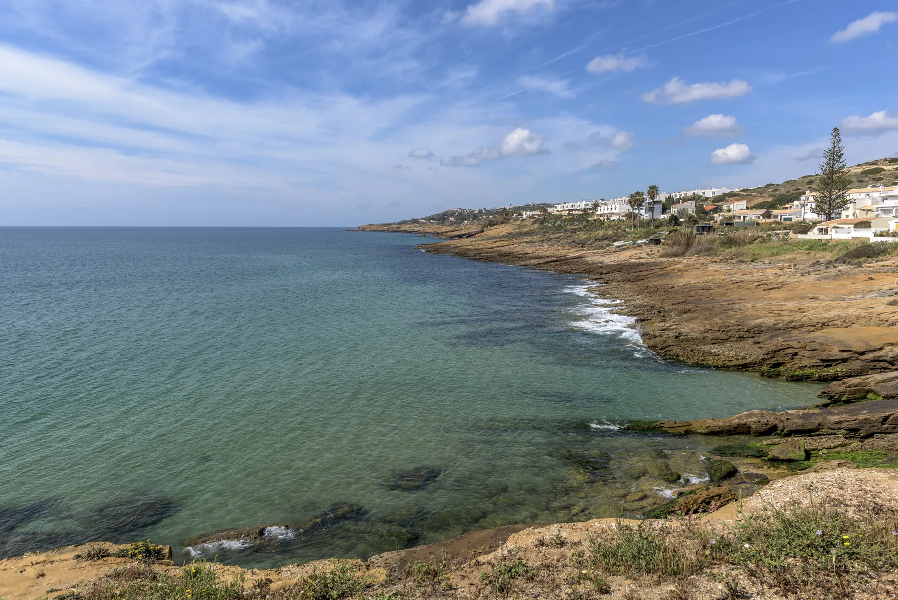Costa con agua clara, afloramientos rocosos y edificios en la ladera.