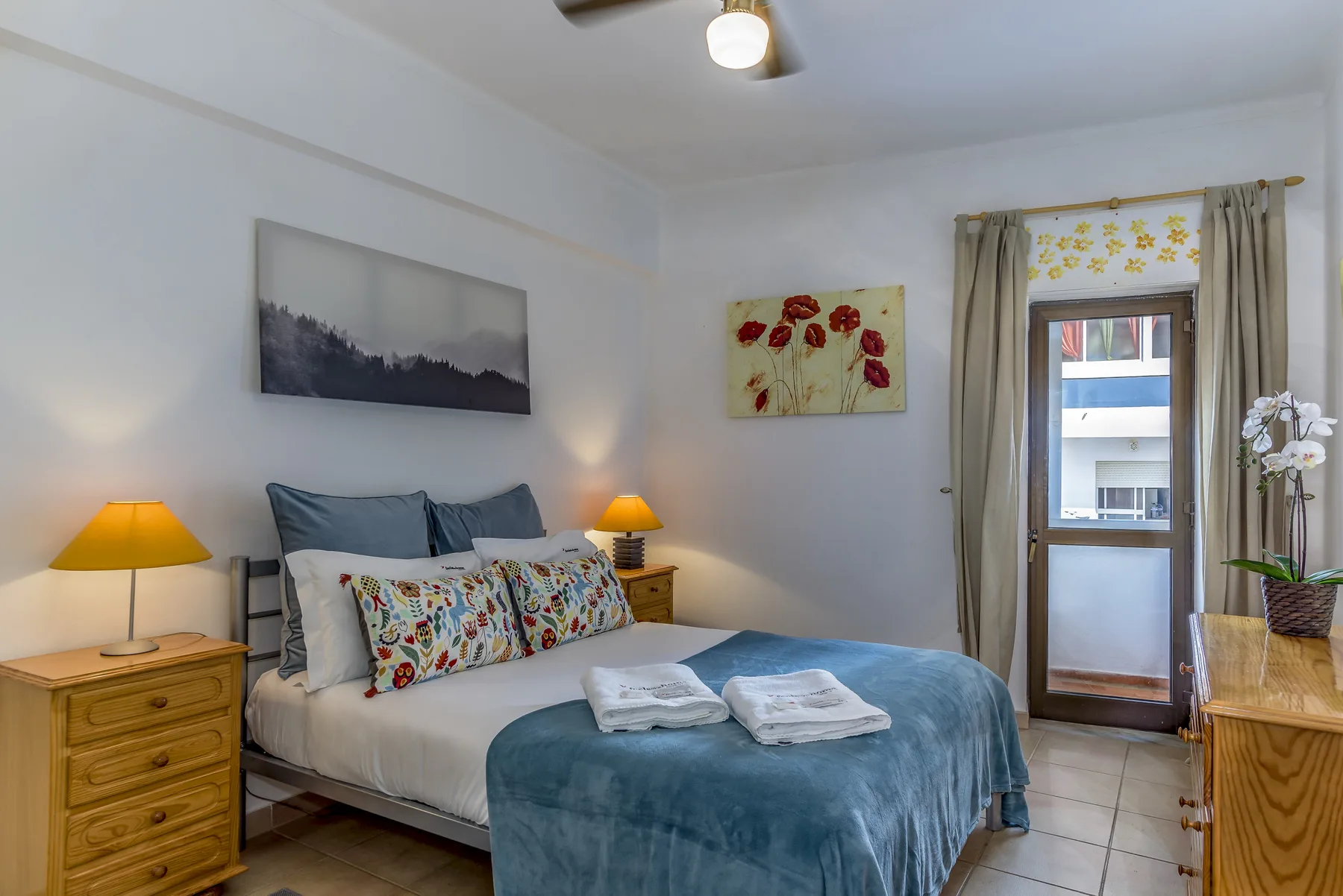 Un dormitorio con una cama, mesillas de noche y una puerta de cristal que da a un balcón.