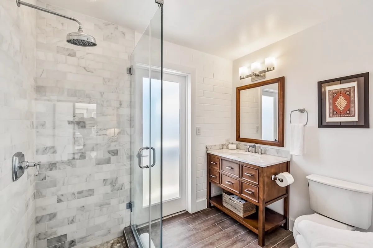 Un baño luminoso con ducha de vidrio, tocador de madera e inodoro.