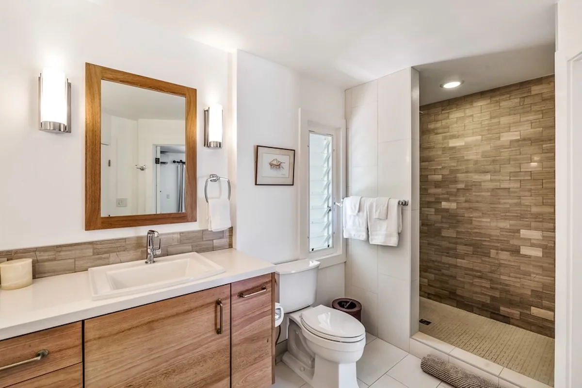 Un baño con mueble de madera, inodoro y ducha a ras de suelo.