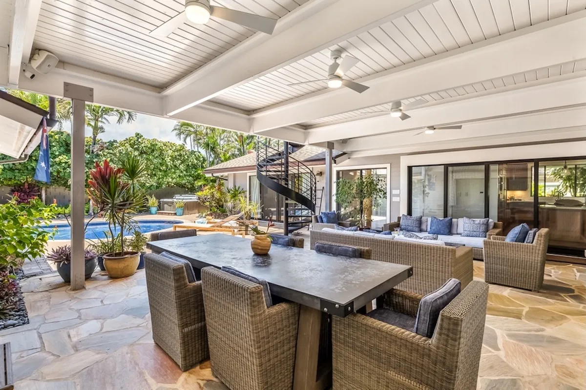 Una zona cubierta de comedor y asientos da a una piscina y un jardín.