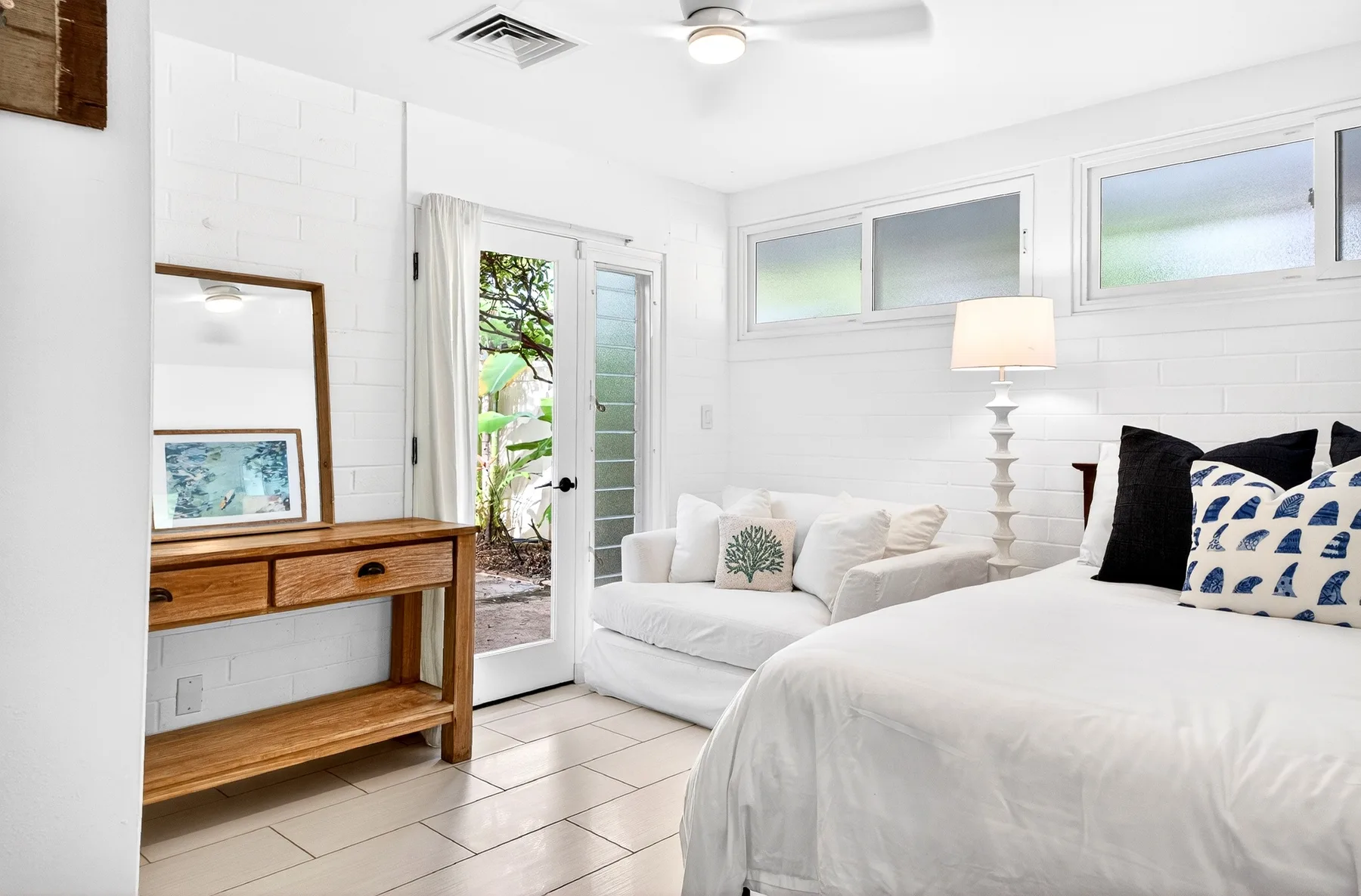 Un dormitorio luminoso con cama, asientos y una puerta de vidrio abierta a un patio.