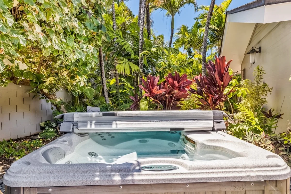 Un jacuzzi exterior está rodeado de plantas tropicales junto a un edificio.