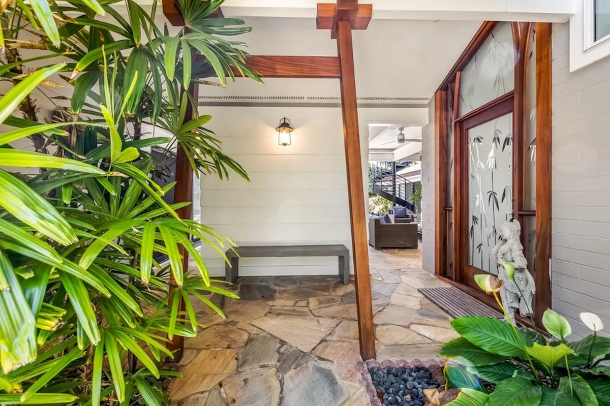 Una entrada cubierta con pavimento de piedra, vigas de madera y plantas frondosas.