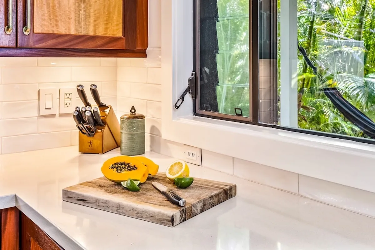 Una encimera de cocina con una tabla de cortar y fruta junto a una ventana abierta.
