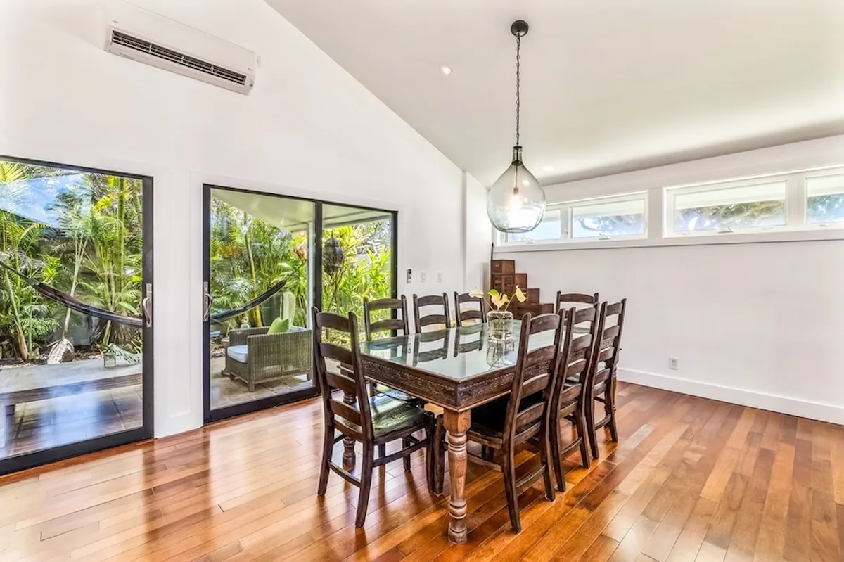 Un comedor con una mesa de madera y sillas junto a grandes ventanas.