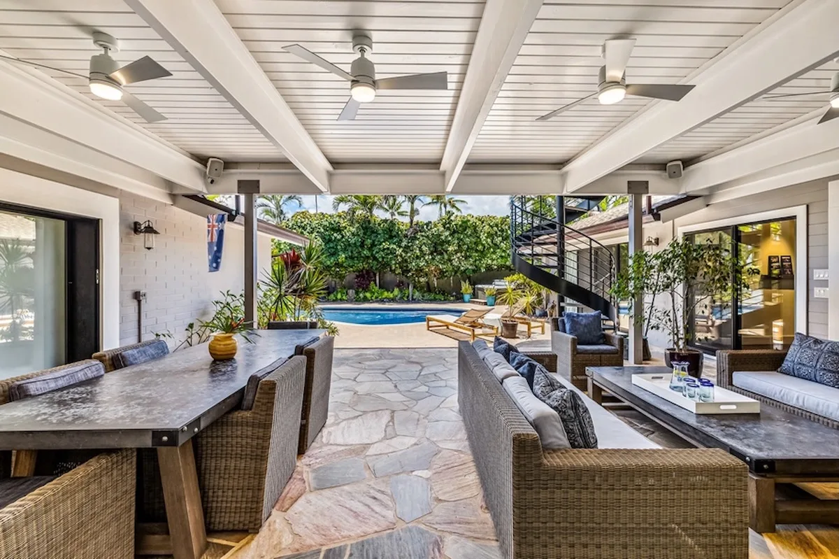 Patio cubierto con comedor y asientos de descanso junto a una piscina.