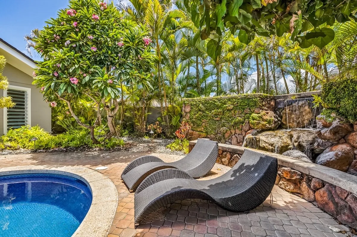 Un patio ajardinado junto a la piscina, con asientos curvos y plantas tropicales.