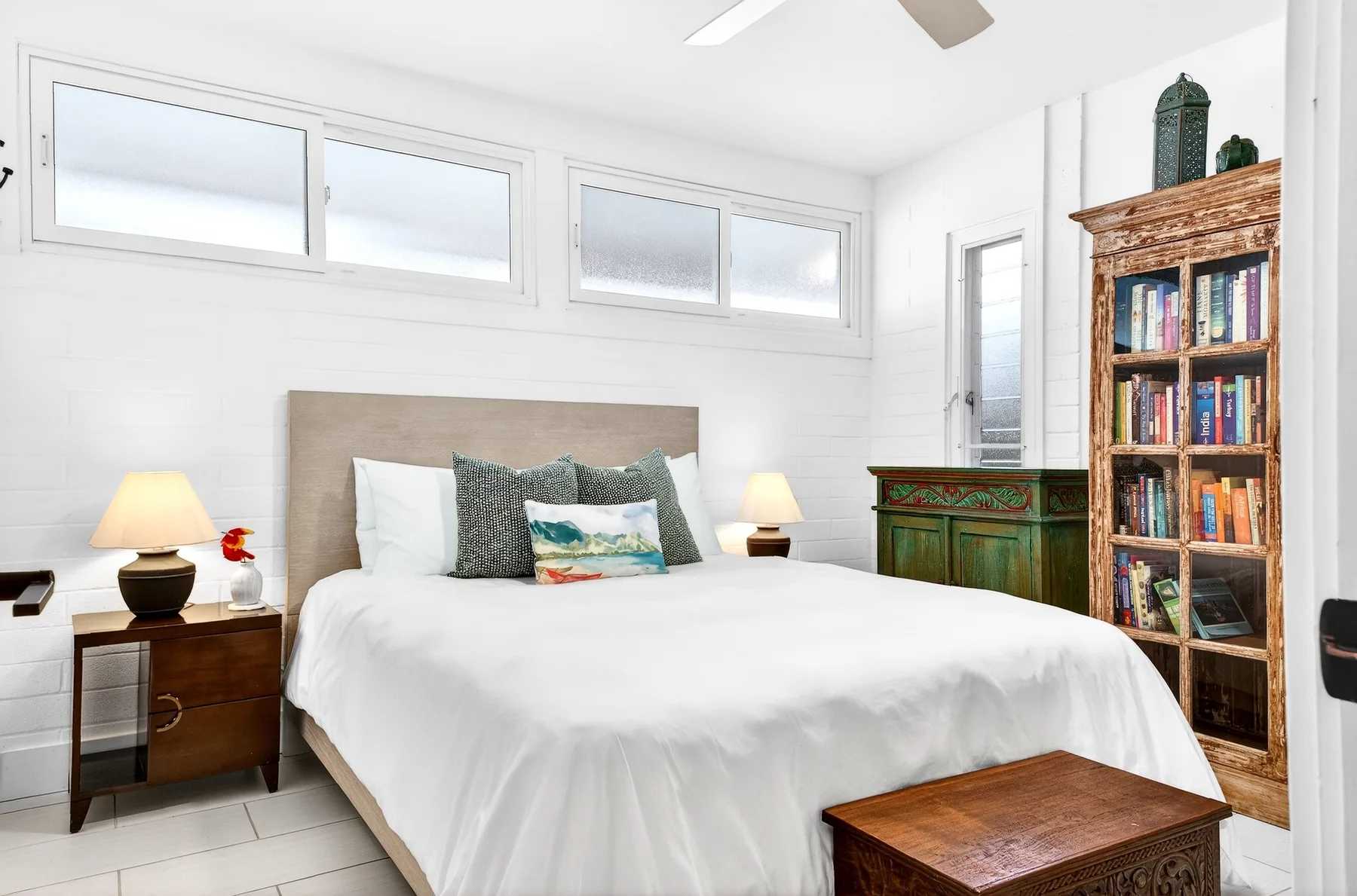 Un dormitorio luminoso con una cama bien tendida, mesitas de noche y una estantería.