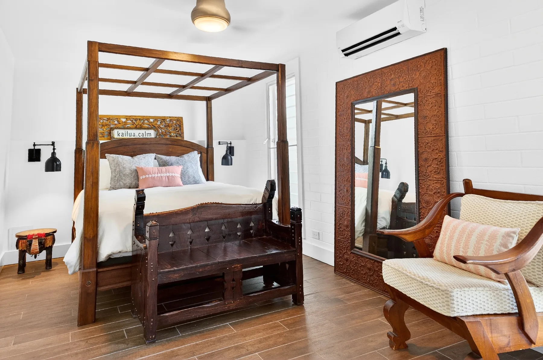 Un dormitorio con una cama con dosel de madera y un sillón acolchado junto a un espejo.