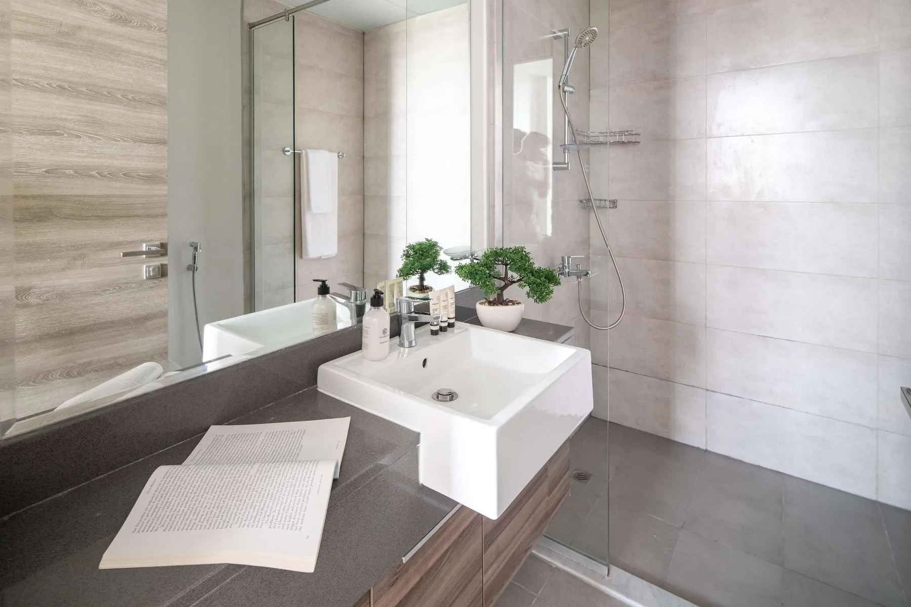 Un baño moderno con lavabo blanco, encimera y ducha de cristal.