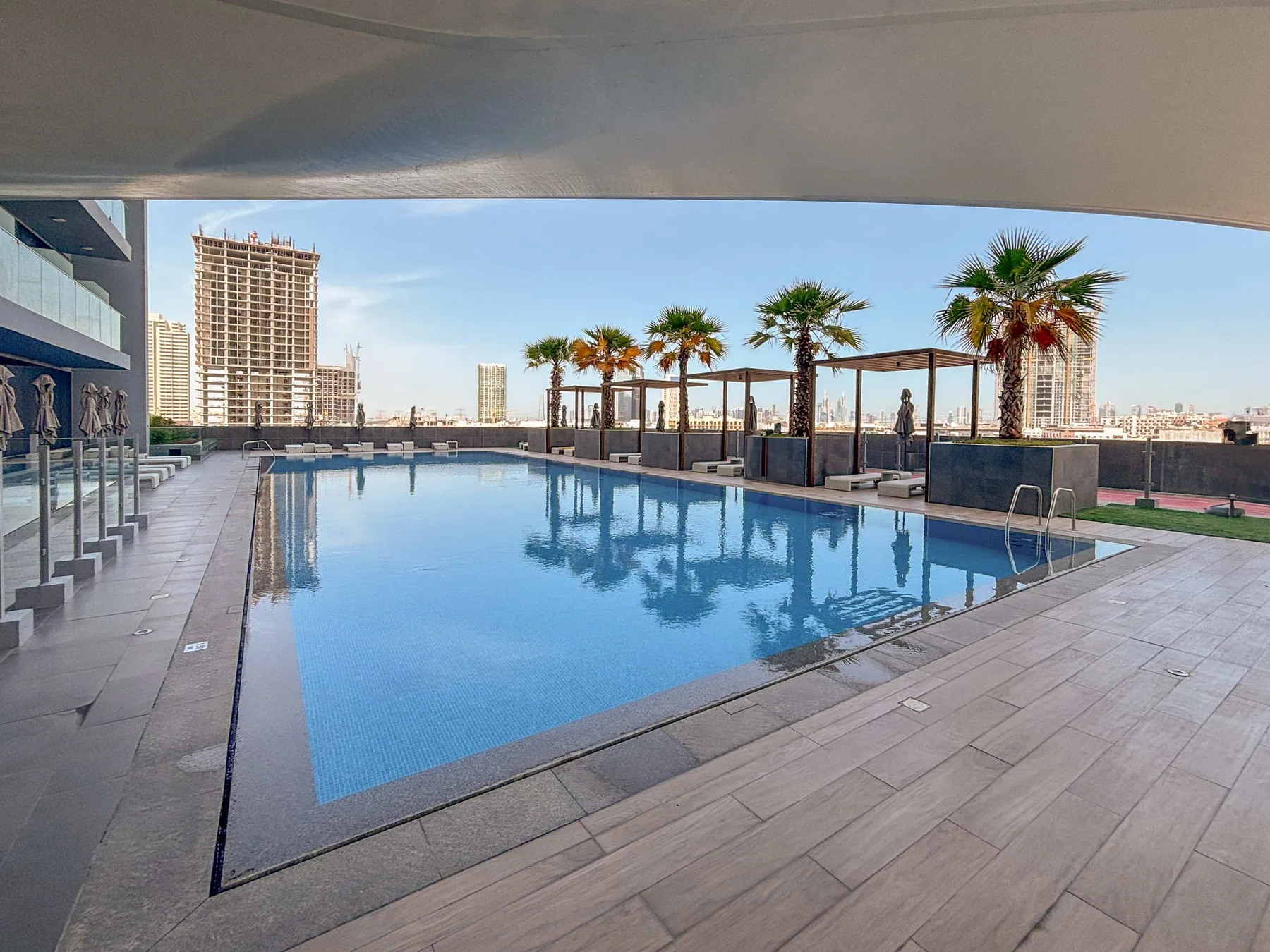 Una piscina en la azotea está junto a una terraza embaldosada, con palmeras al fondo.