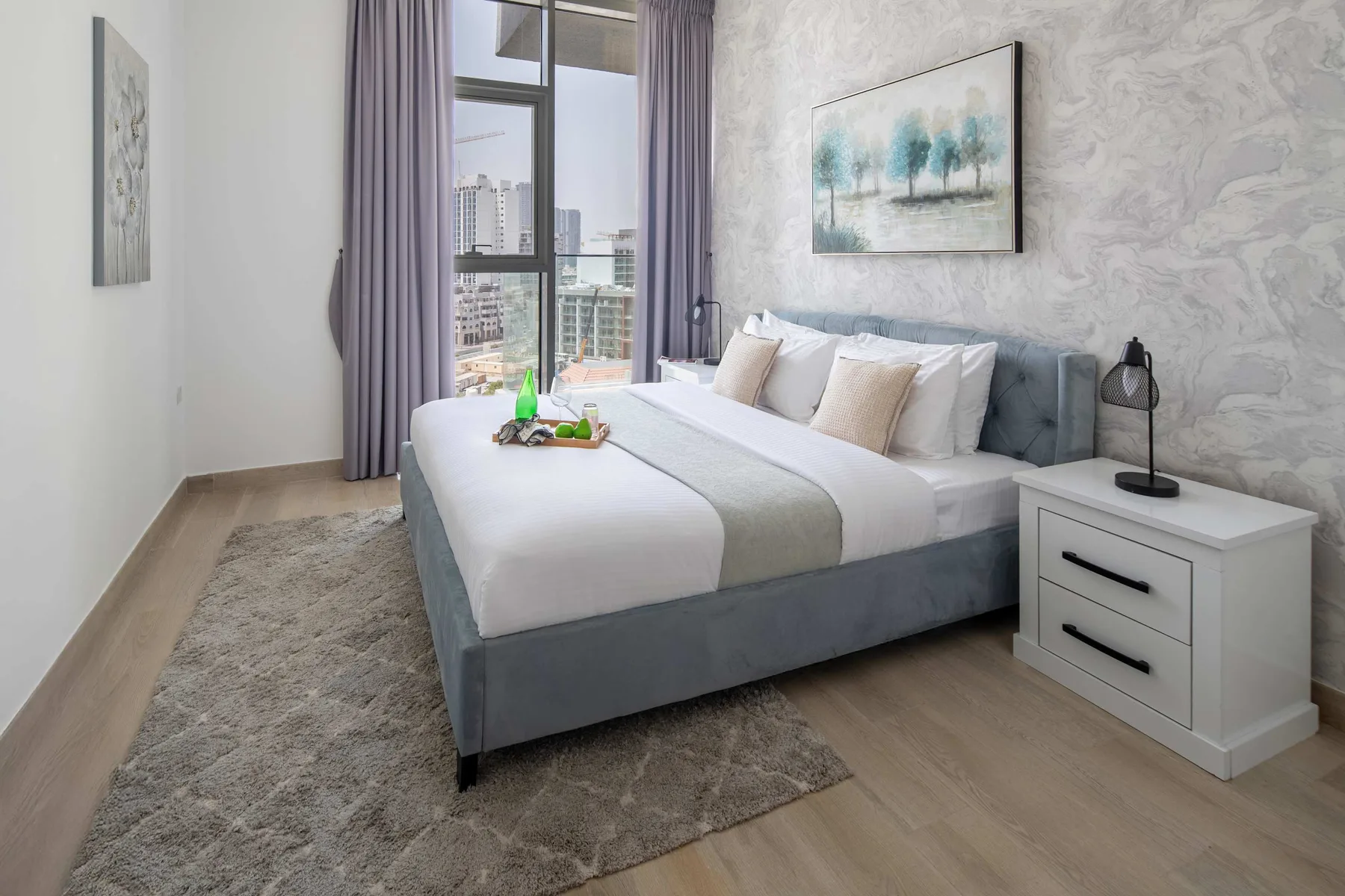 Un dormitorio con una cama bien tendida, una mesita de noche y ventanas grandes.