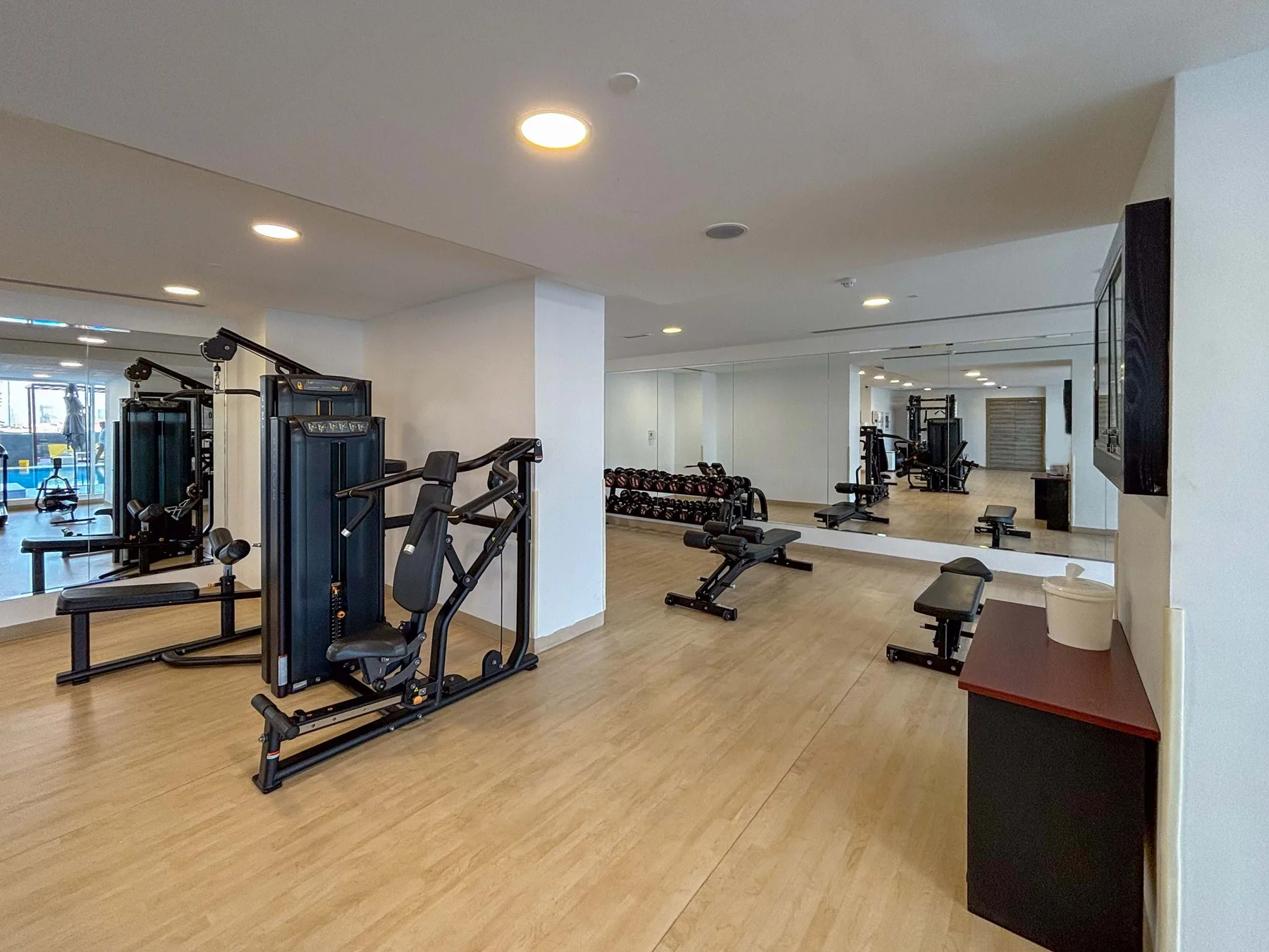 Un gimnasio con máquinas de ejercicio y pesas reflejadas en un espejo de pared.