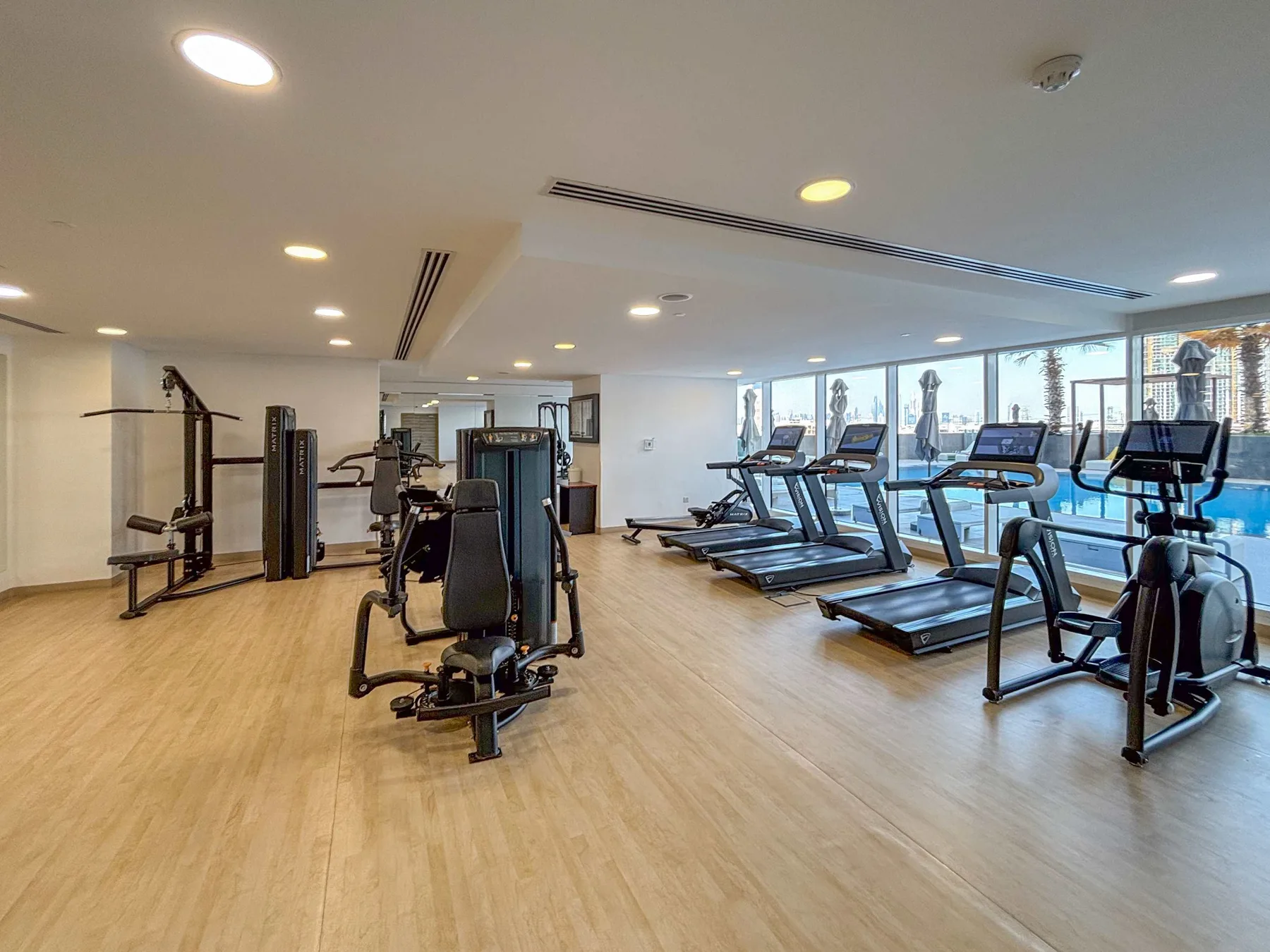 Una sala de ejercicio luminosa con máquinas y cintas de correr junto a grandes ventanas.