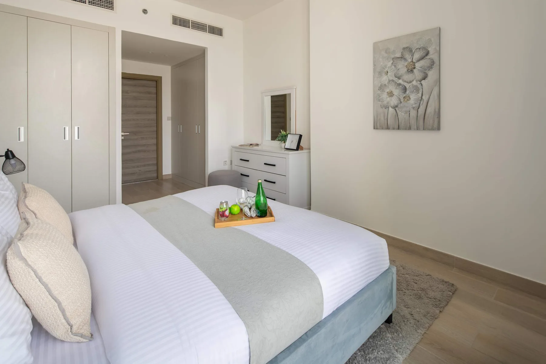 Un dormitorio luminoso con una cama bien tendida y un cuadro floral.