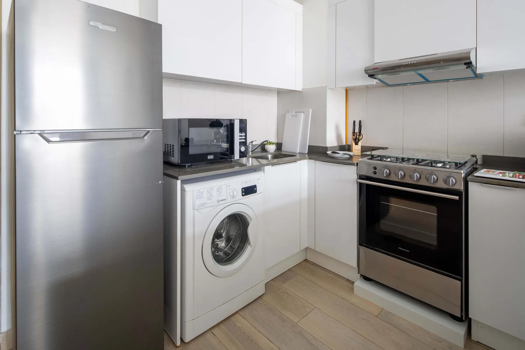 Una cocina compacta con armarios blancos, un refrigerador y electrodomésticos para cocinar.