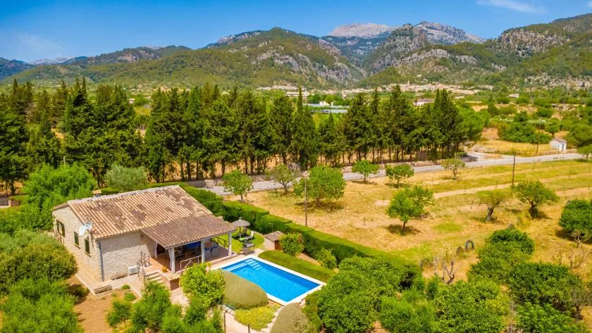 Una propiedad rural con piscina se encuentra entre árboles, campos y montañas.