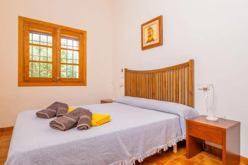 Un dormitorio con una cama de madera, toallas dobladas y una ventana.