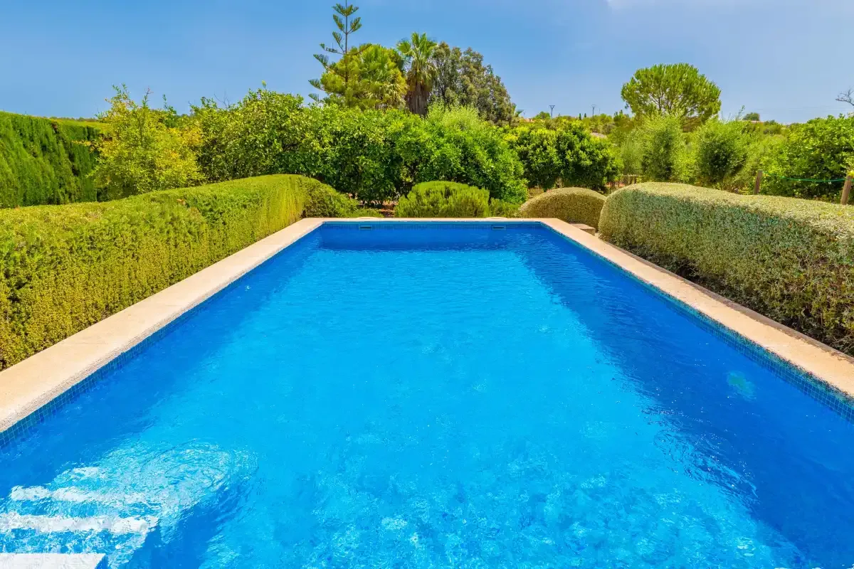 Una piscina está rodeada de setos recortados y árboles.