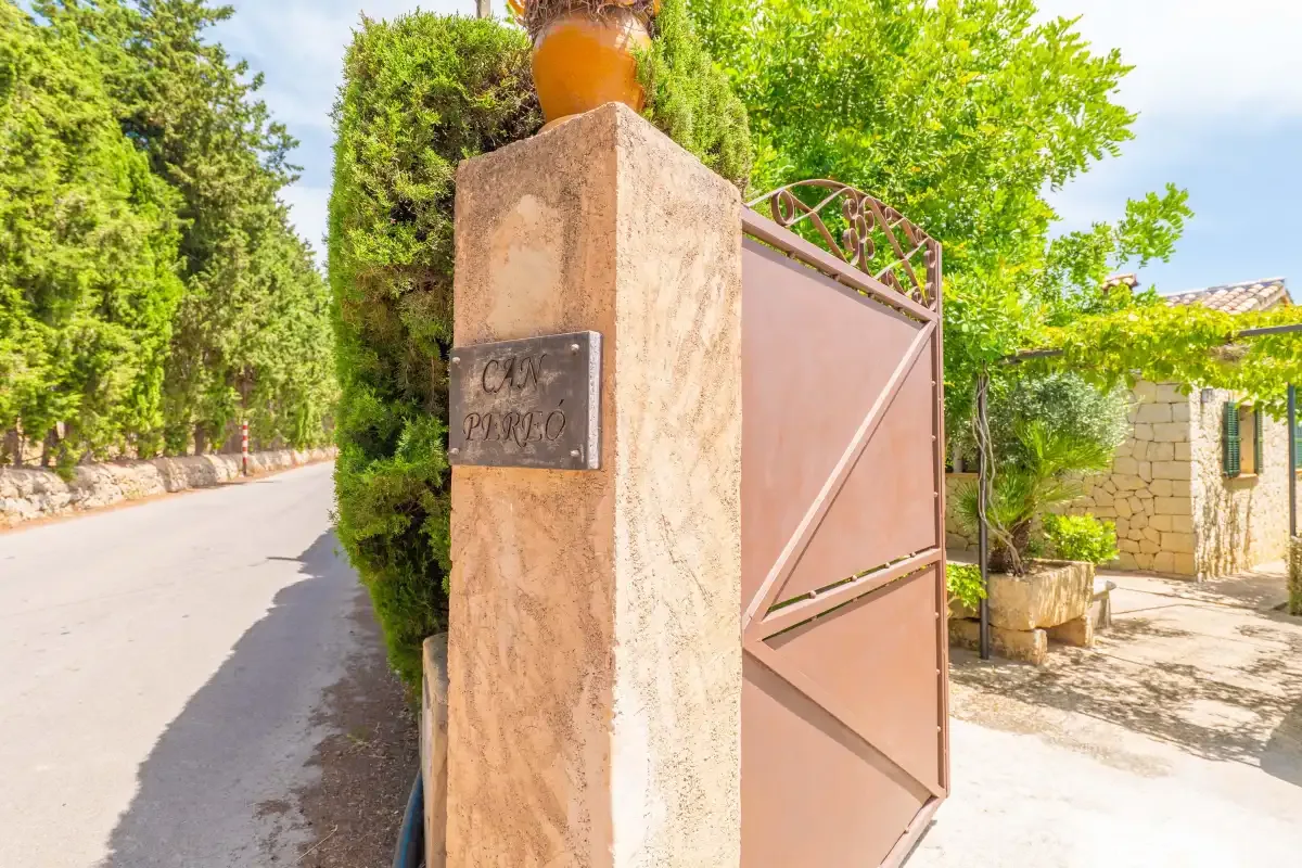 Una puerta metálica abierta está junto a un pilar de piedra, en un camino arbolado.