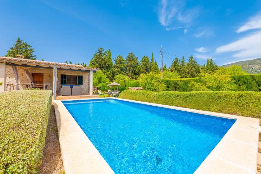 Una piscina al aire libre está junto a un edificio bajo y setos recortados.