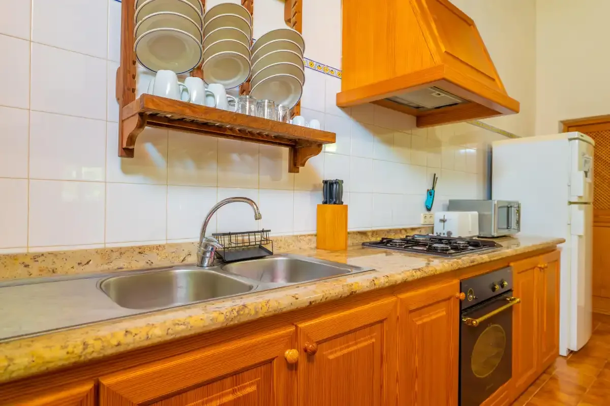 Una cocina con azulejos, encimera, fregadero, fogones y armarios de madera.
