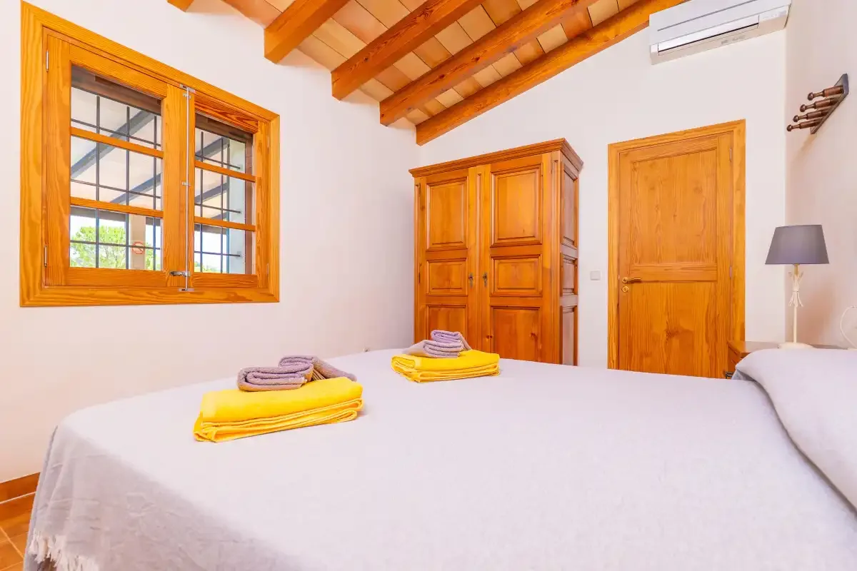 Dormitorio con armario de madera, ventana y toallas dobladas sobre la cama.