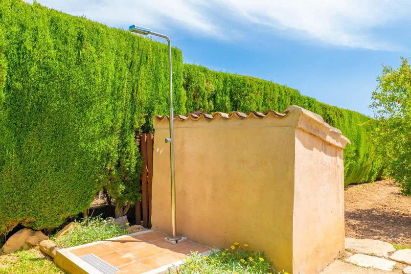 Una ducha exterior está junto a un seto verde alto.