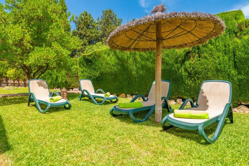 Zona de descanso en un jardín con tumbonas bajo una sombrilla de paja.