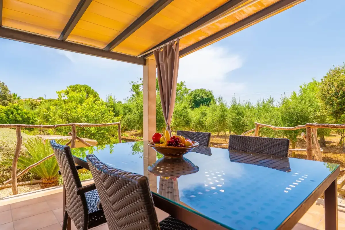 Comedor exterior cubierto con una mesa de vidrio y vistas al jardín.
