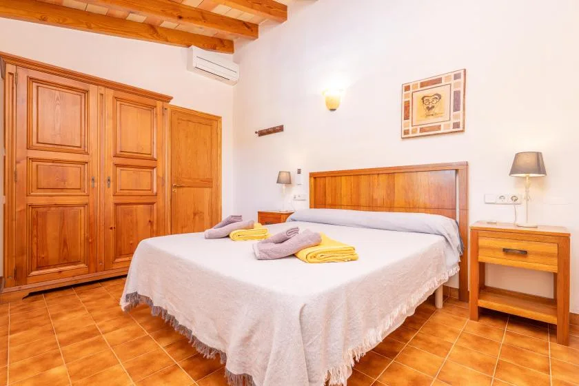 Un dormitorio con cama y armarios de madera y suelo de baldosas color terracota.