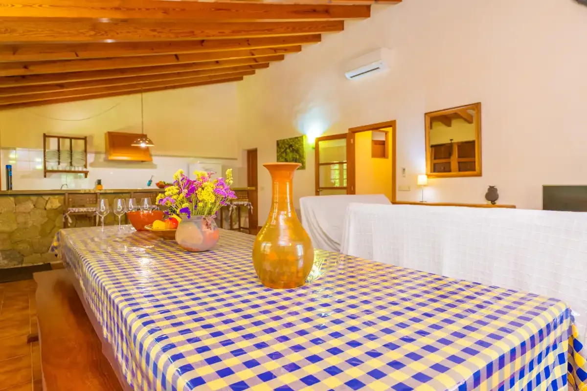Comedor con un mantel a cuadros y una cocina abierta al fondo.