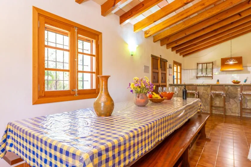 Un comedor con una mesa larga, un mantel colorido y vigas de madera expuestas.