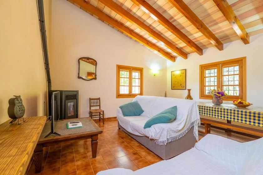 Sala de estar con un sofá cubierto, vigas de madera y ventanas iluminadas.