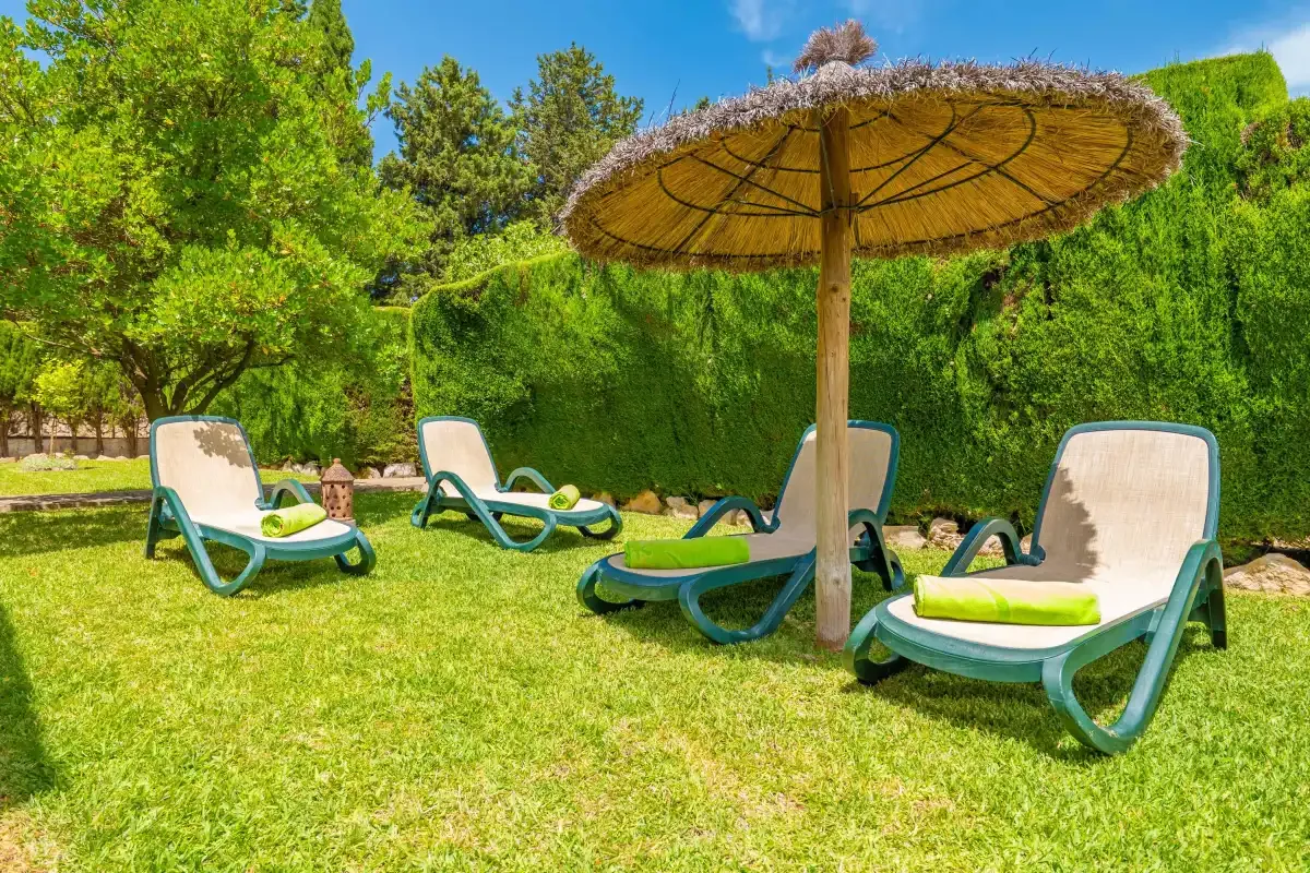 Una zona de descanso en el jardín con tumbonas bajo una gran sombrilla.
