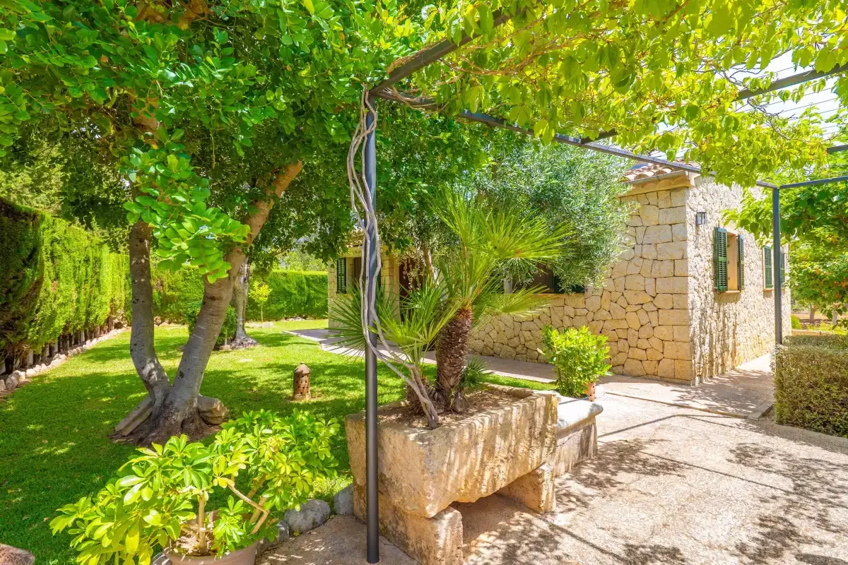 Un patio ajardinado y frondoso con un sendero de piedra junto a un pequeño edificio de piedra.