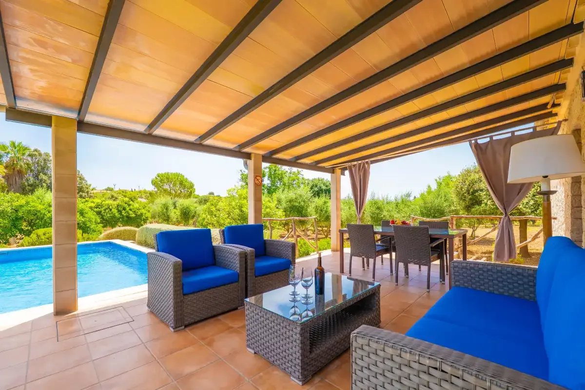 Un patio cubierto con asientos al aire libre da a una piscina y vegetación.