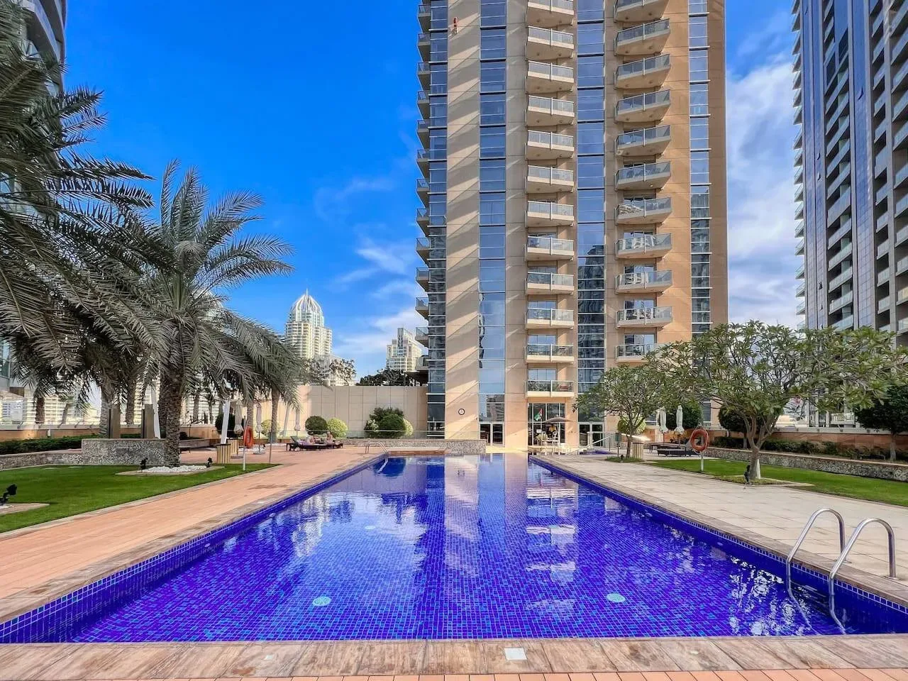 Una piscina azul está rodeada de palmeras y edificios altos.
