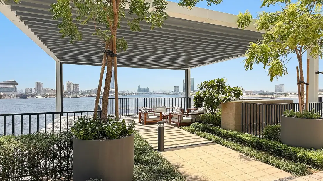 A waterside patio has a covered seating area, planters, and views across the water.