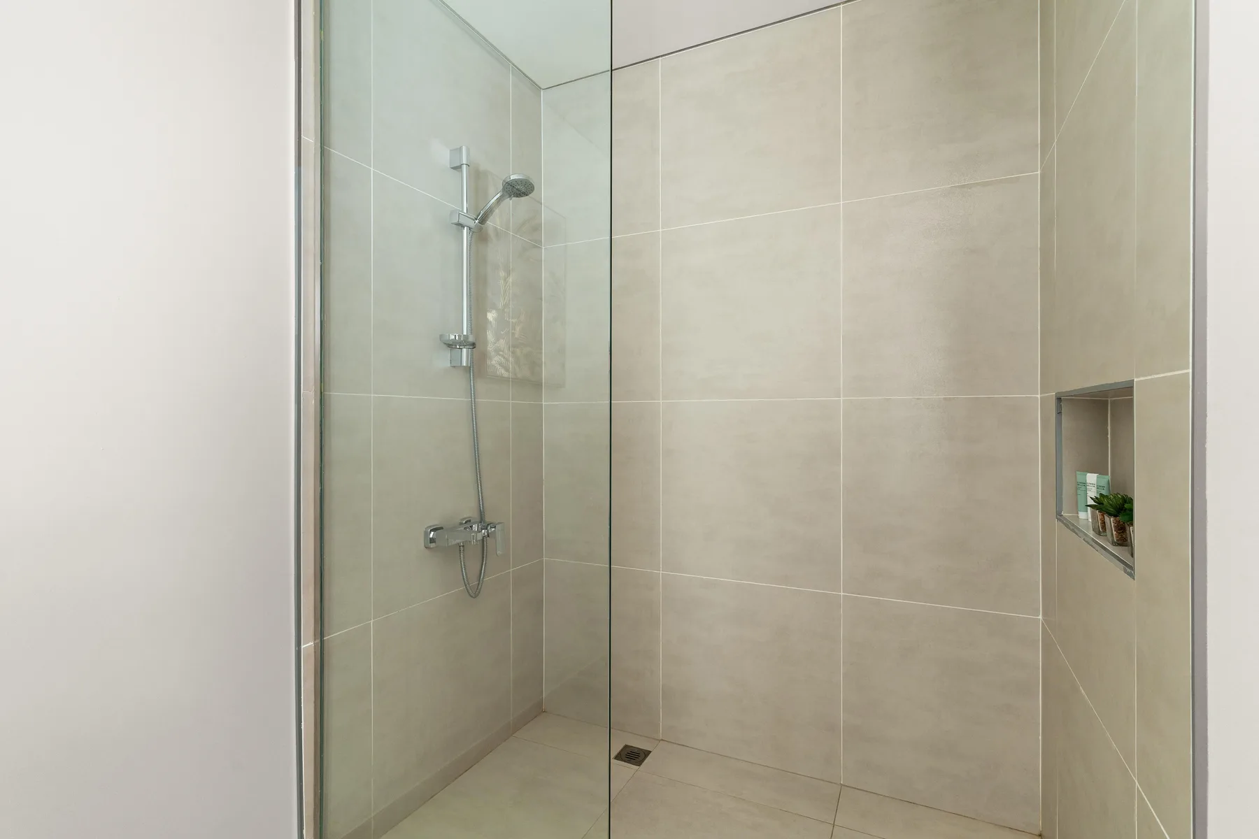 A tiled shower with a glass panel and a small recessed wall shelf.