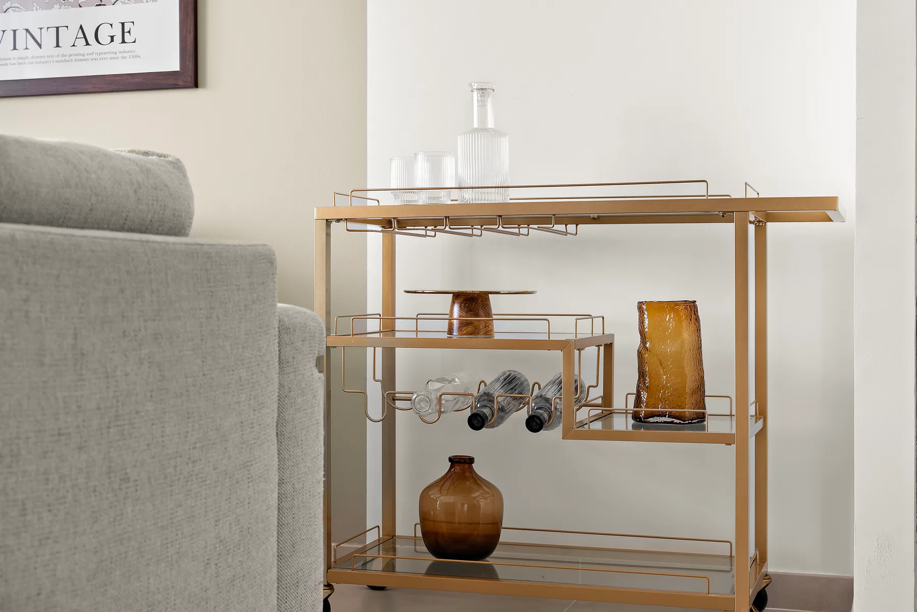 A living room with a gold-toned bar cart holding glassware and bottles.