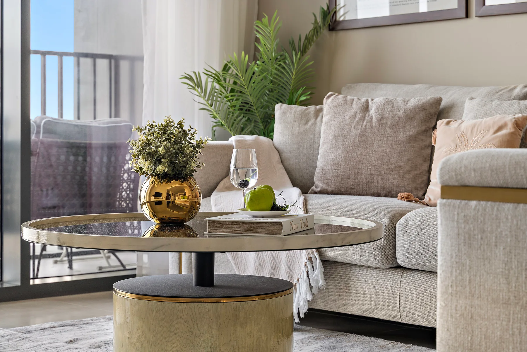 A bright living room with a sofa, a round coffee table, and leafy plants.
