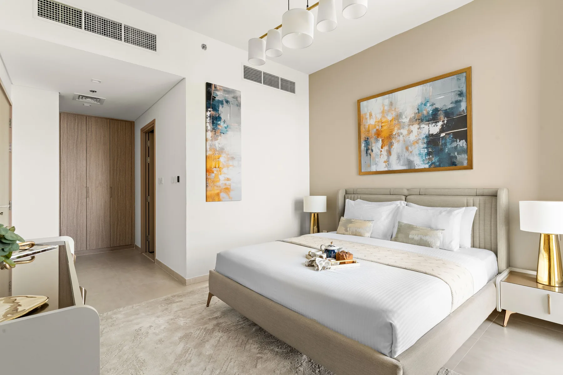 A bright bedroom with a neatly made bed beneath abstract wall art.