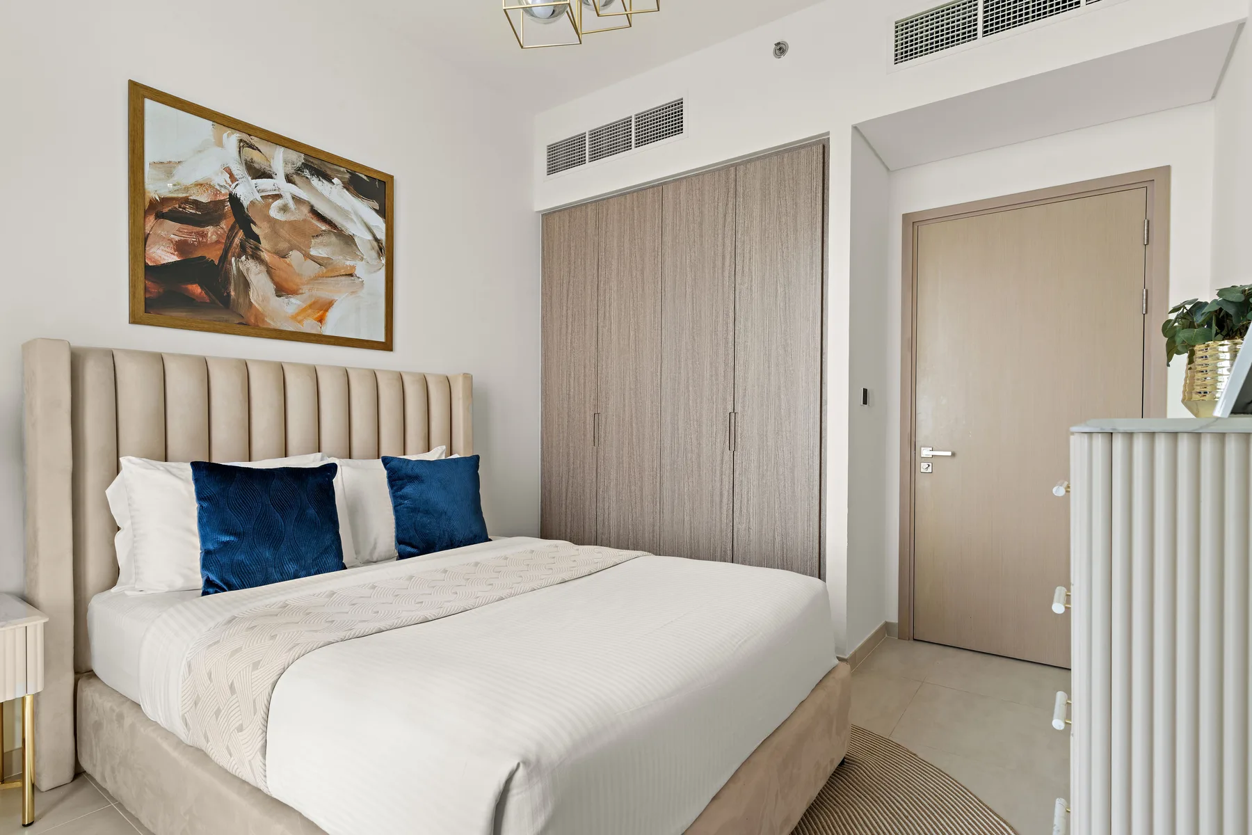A bedroom with a neatly made bed and a framed abstract painting above it.